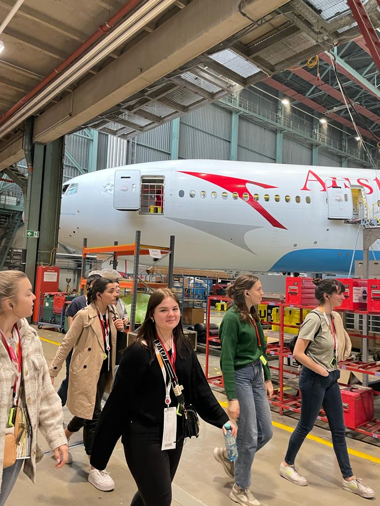 Studierende im Technikbereich der Austria Airlines. Im Hintergrund ist ein stehendes Flugzeug der Austrian Airlines zu sehen.