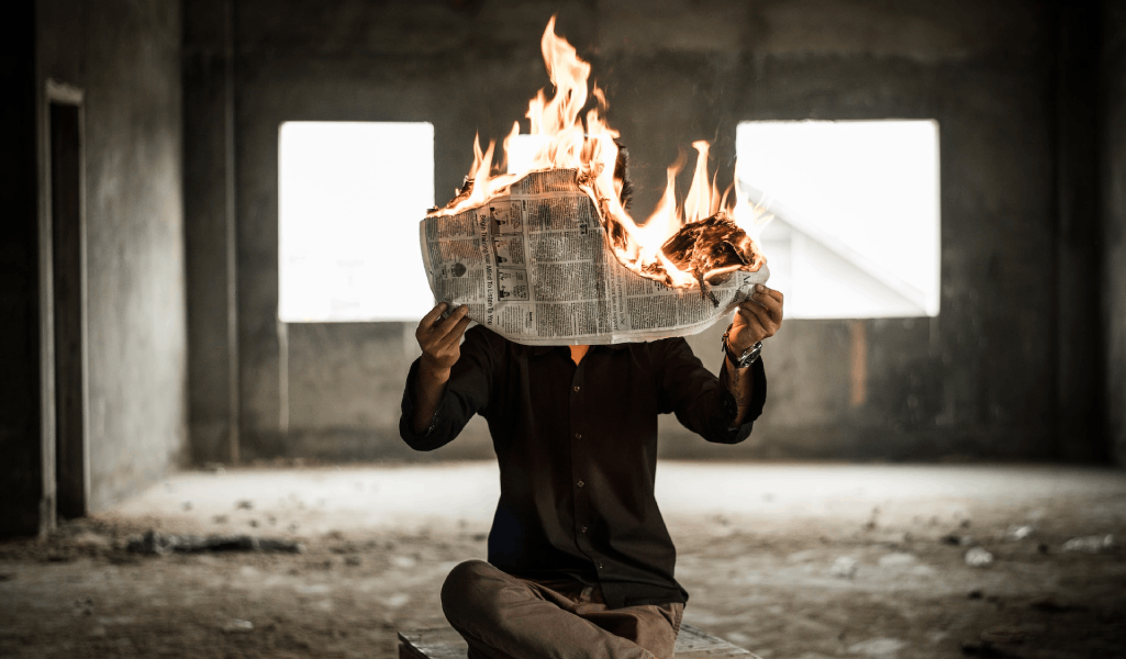 Eine Person hält eine brennende Zeitung vor ihr Gesicht.